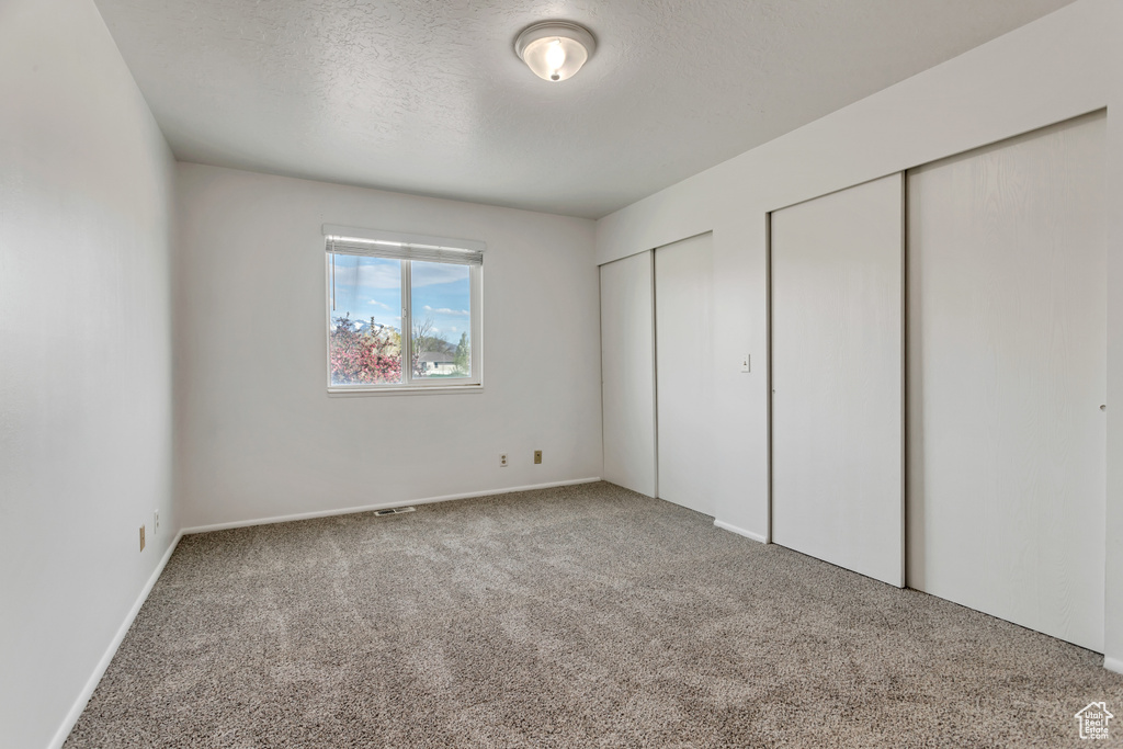 Unfurnished bedroom featuring light carpet, a textured ceiling, and multiple closets