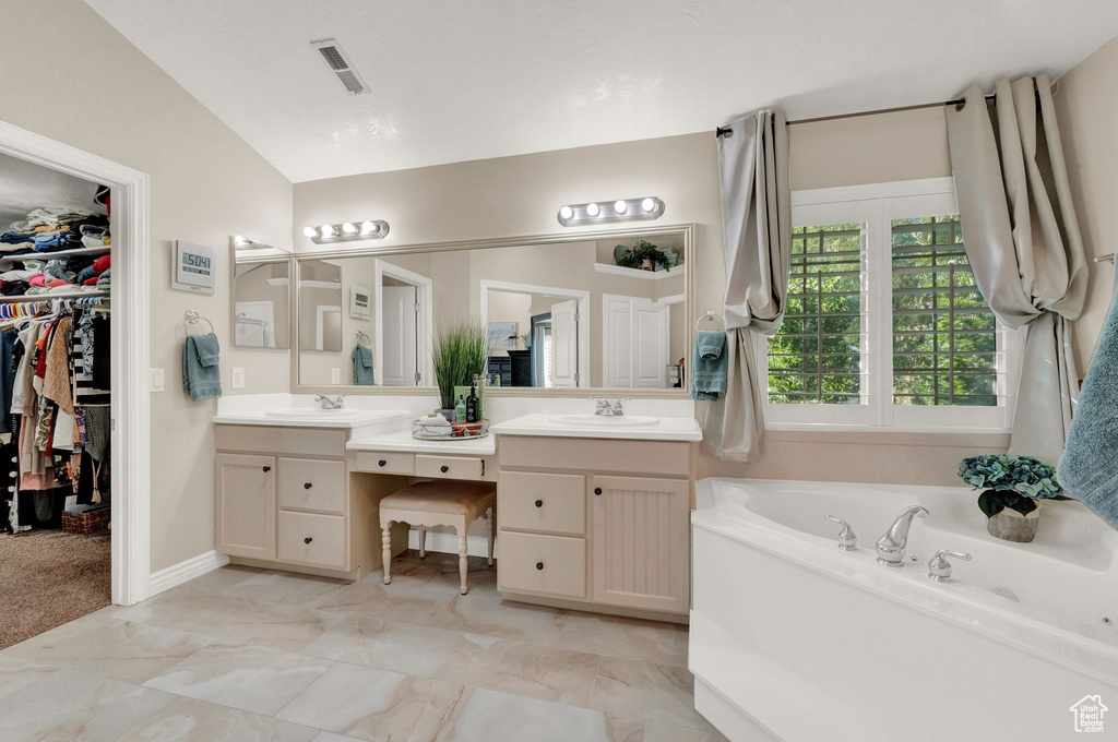 Bathroom with lofted ceiling, a washtub, dual vanity, and tile flooring