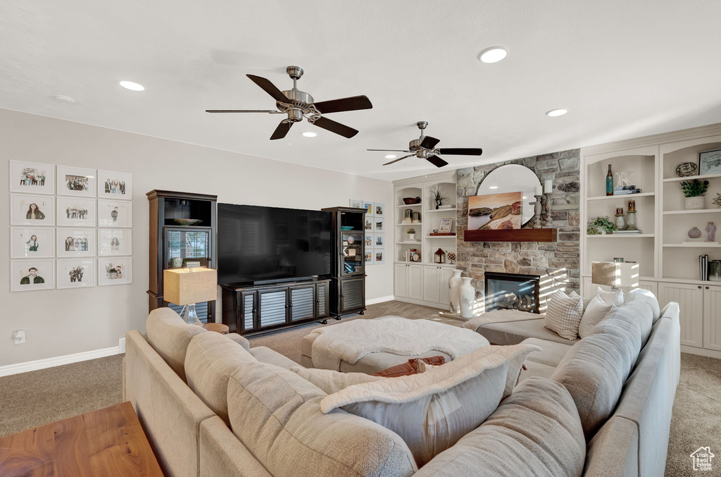 Living room with light carpet, ceiling fan, a fireplace, and built in shelves
