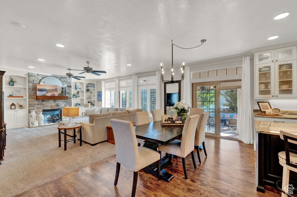 Dining area featuring a fireplace, a textured ceiling, ceiling fan with notable chandelier, built in features, and light hardwood / wood-style flooring