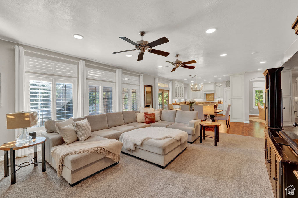 Living room with ceiling fan with notable chandelier, a textured ceiling, light carpet, and crown molding