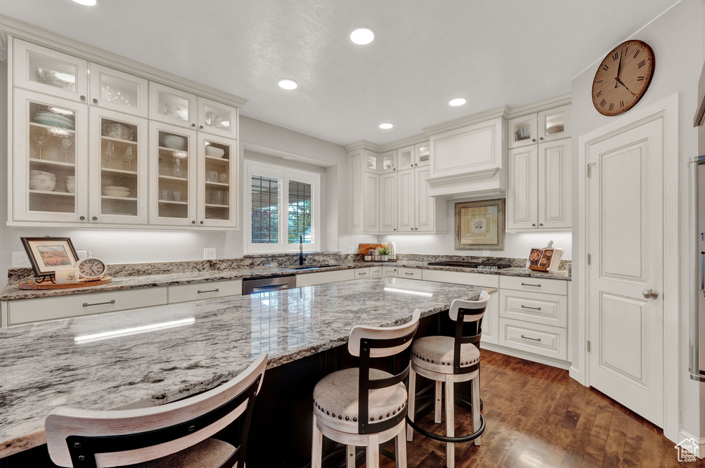 Kitchen with white cabinets, light stone counters, dark hardwood / wood-style flooring, and a kitchen bar