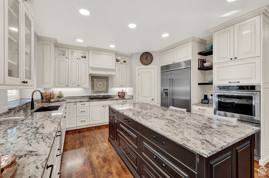 Kitchen with appliances with stainless steel finishes, dark brown cabinetry, sink, and light stone counters