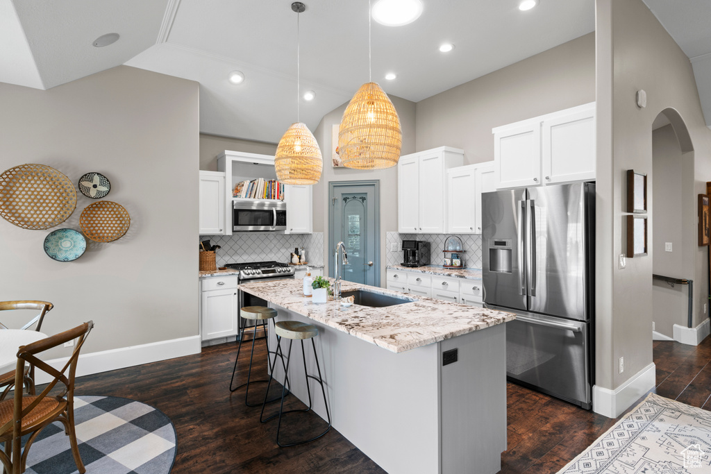 Kitchen with appliances with stainless steel finishes, hanging light fixtures, tasteful backsplash, an island with sink, and dark hardwood / wood-style flooring
