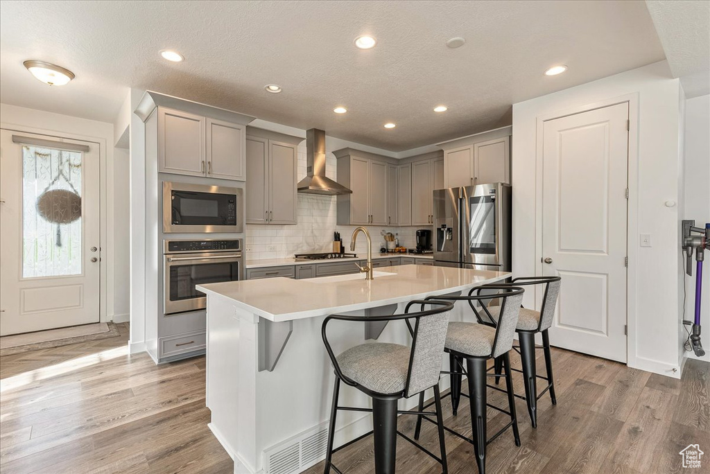 Kitchen featuring stainless steel appliances, light hardwood / wood-style floors, wall chimney exhaust hood, and a kitchen bar