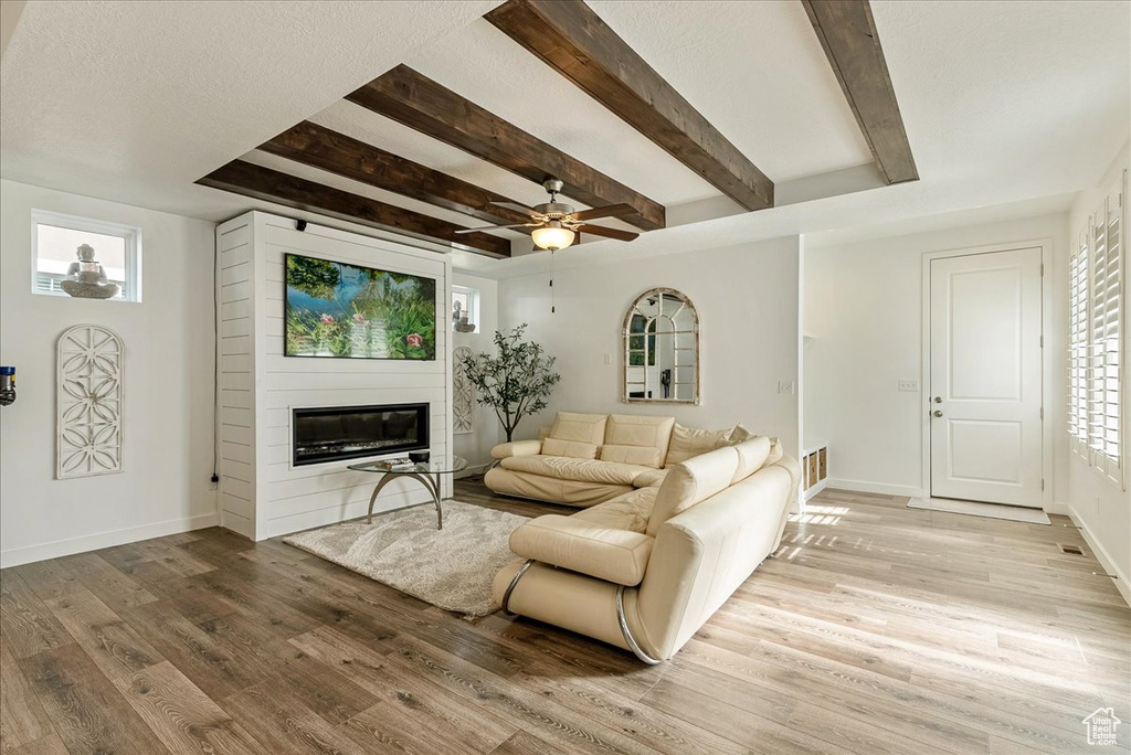 Living room with a healthy amount of sunlight, ceiling fan, a large fireplace, and light wood-type flooring