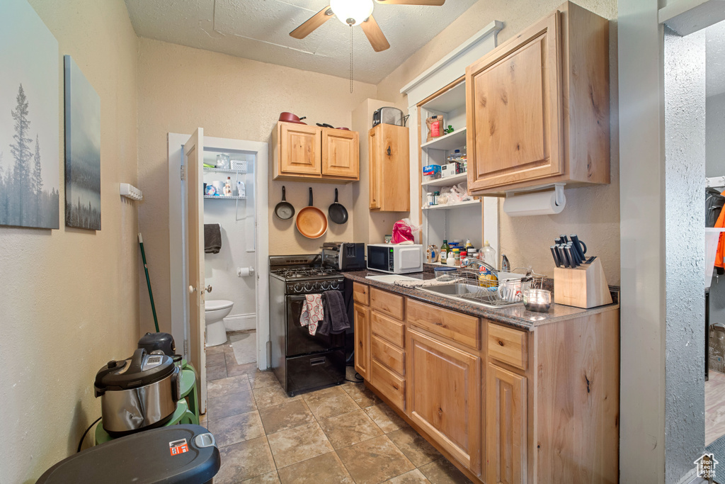 Kitchen featuring gas stove, sink, ceiling fan, and light tile floors
