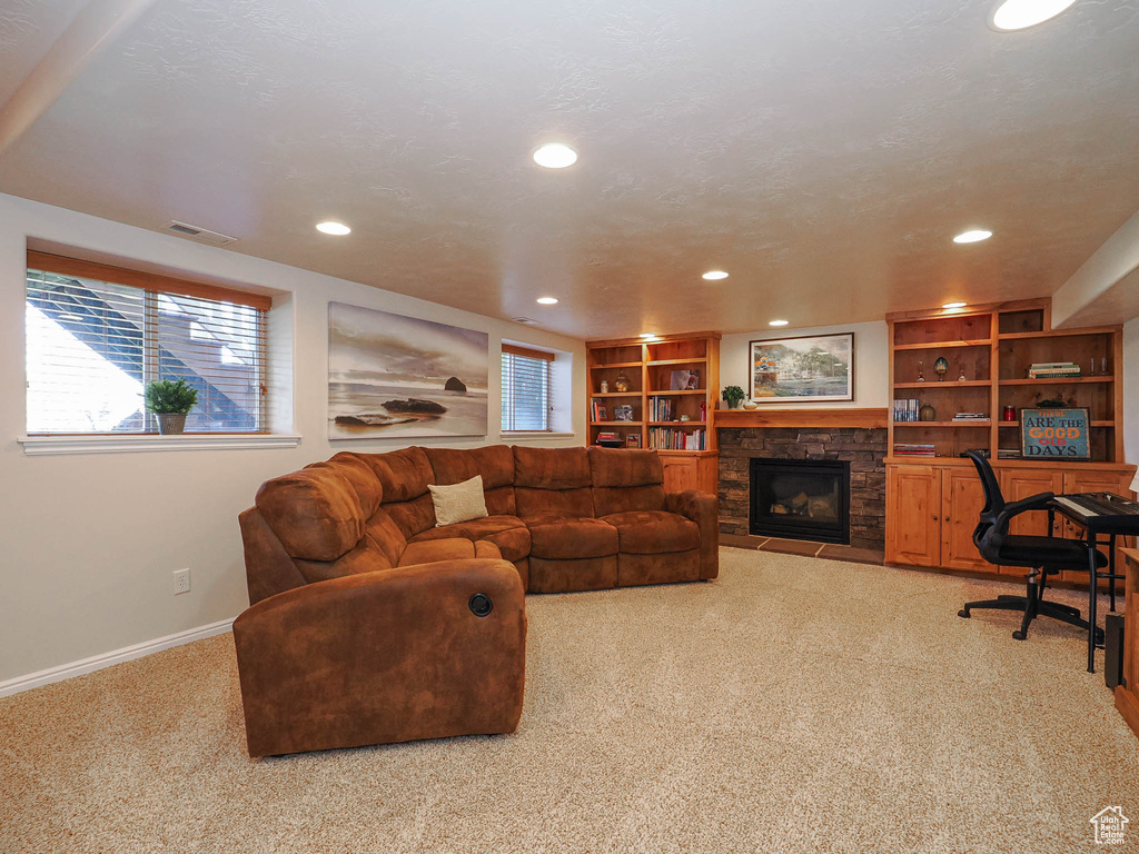 Living room featuring built in shelves, a stone fireplace, and light carpet
