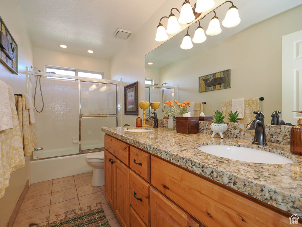 Full bathroom with tile flooring, double vanity, combined bath / shower with glass door, and toilet