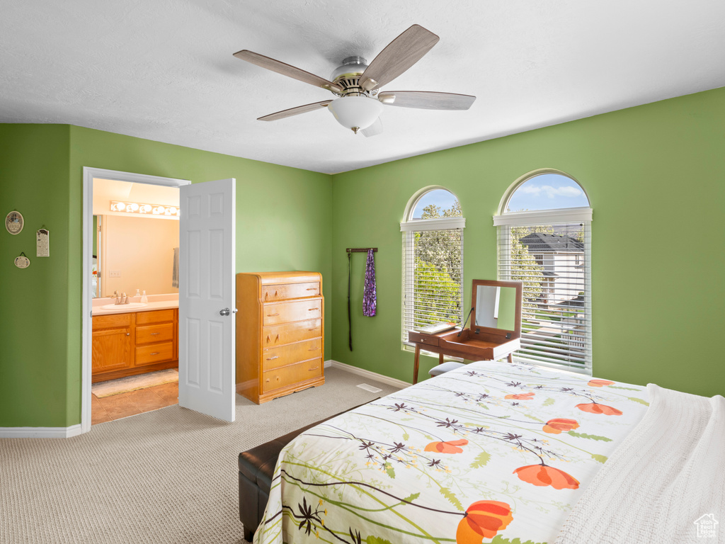 Carpeted bedroom with ensuite bathroom, ceiling fan, sink, and multiple windows