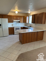 Kitchen featuring sink, white appliances, kitchen peninsula, and light tile flooring
