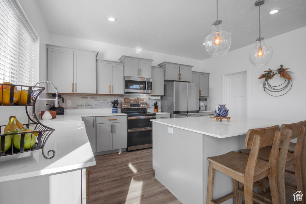 Kitchen featuring appliances with stainless steel finishes, backsplash, hardwood / wood-style flooring, pendant lighting, and a breakfast bar