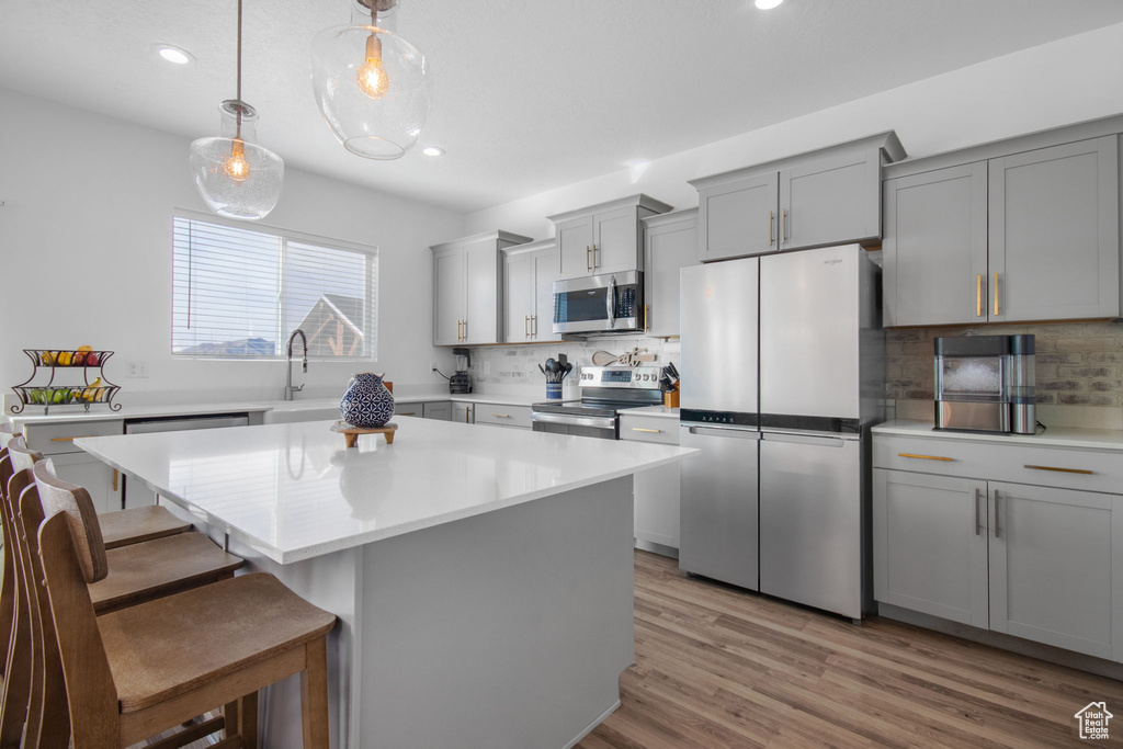 Kitchen featuring a kitchen island, tasteful backsplash, light wood-type flooring, and stainless steel appliances