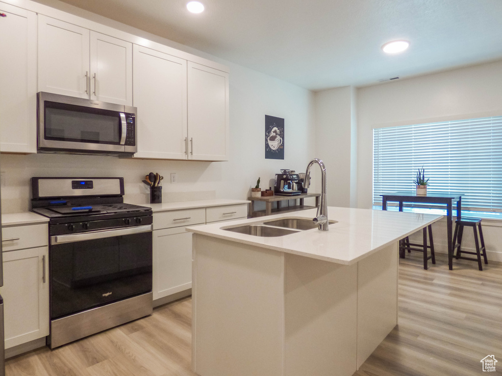 Kitchen with stainless steel appliances, white cabinetry, light wood-type flooring, and a center island with sink