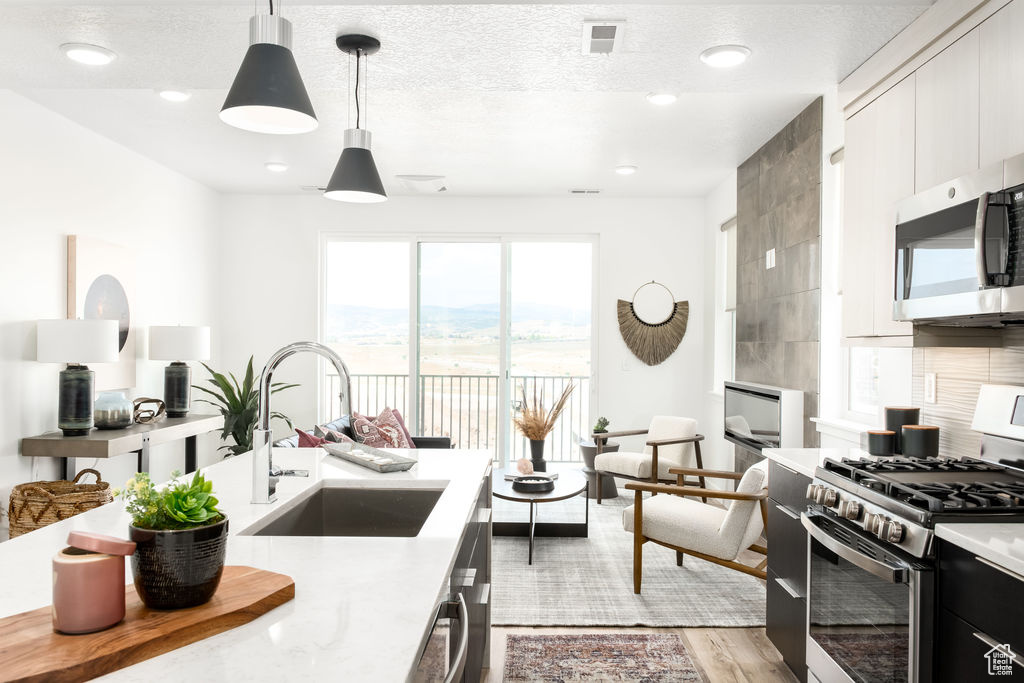 Kitchen with hanging light fixtures, light hardwood / wood-style flooring, stainless steel appliances, white cabinetry, and sink