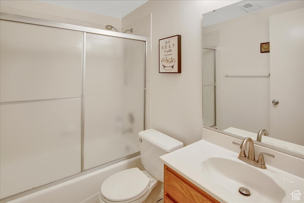 Full bathroom featuring combined bath / shower with glass door, vanity, and toilet