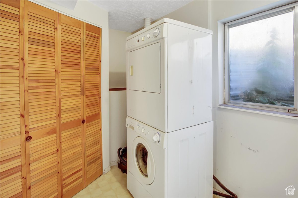 Washroom with a textured ceiling, stacked washer and dryer, and light tile floors