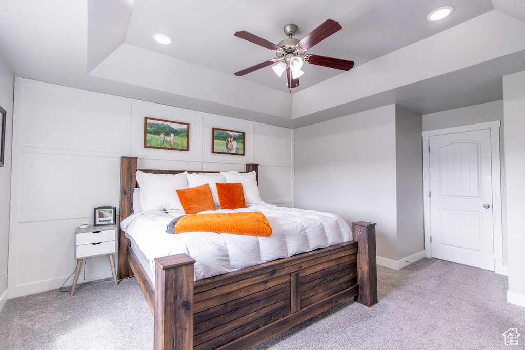 Bedroom featuring a tray ceiling, ceiling fan, and light carpet