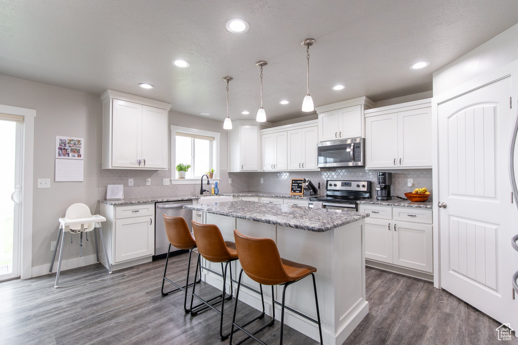Kitchen featuring decorative light fixtures, appliances with stainless steel finishes, dark wood-type flooring, white cabinets, and a center island
