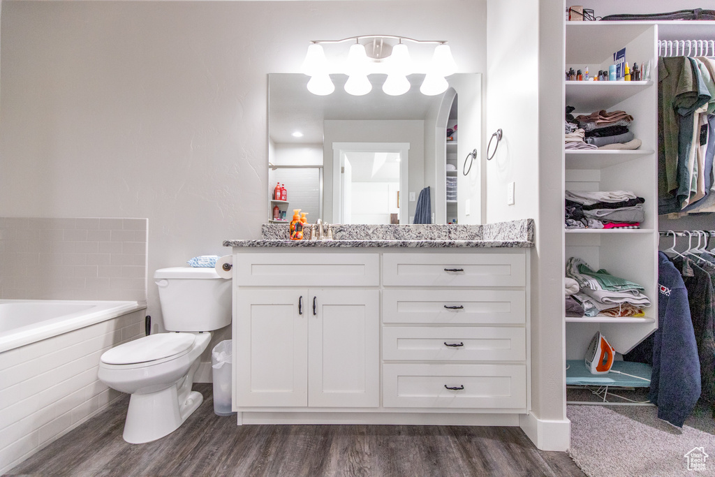 Bathroom featuring hardwood / wood-style flooring, a relaxing tiled bath, toilet, and vanity