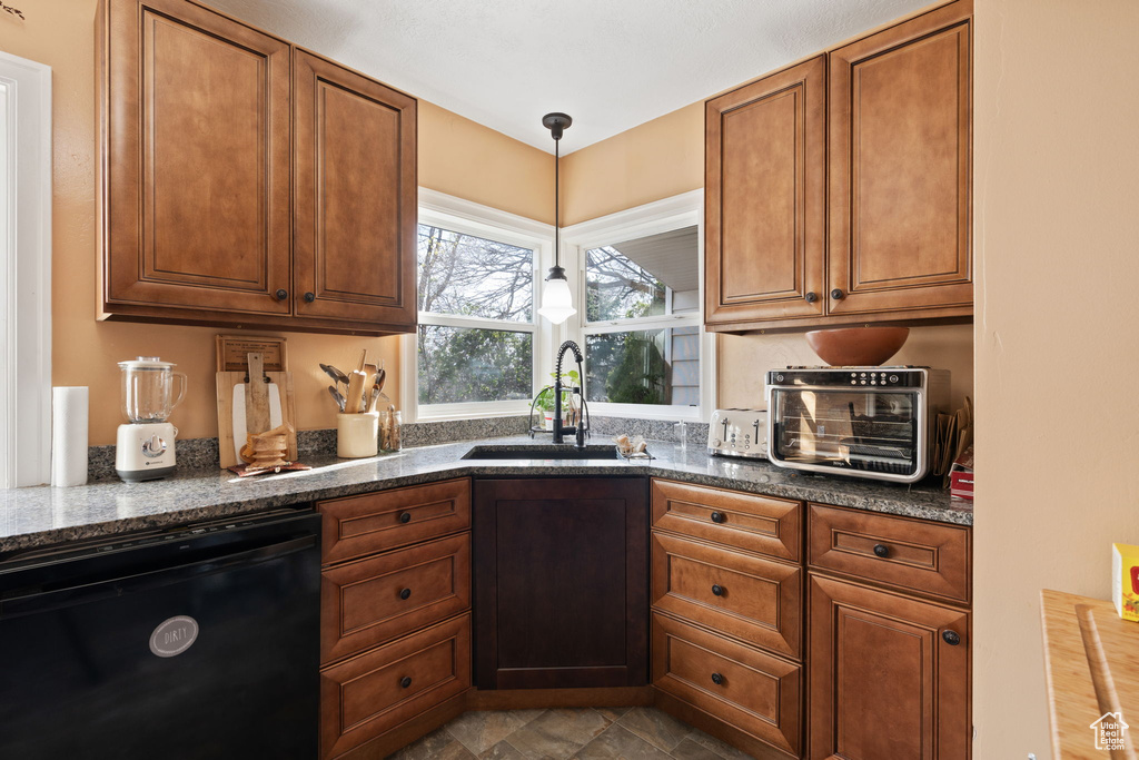 Kitchen featuring hanging light fixtures, light tile flooring, black dishwasher, dark stone countertops, and sink