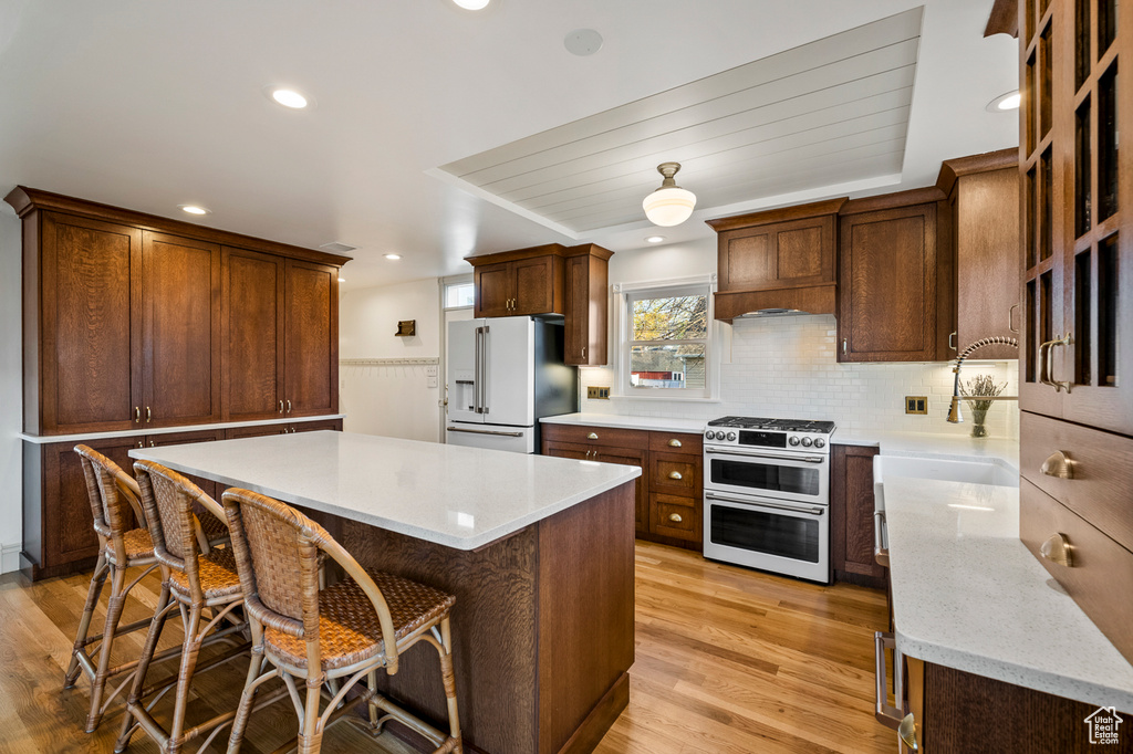 Kitchen with high end appliances, a breakfast bar, light wood-type flooring, backsplash, and a kitchen island