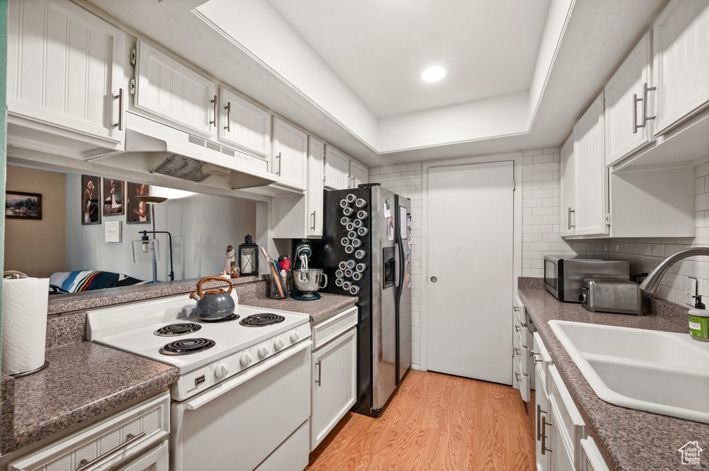 Kitchen featuring white electric stove, a tray ceiling, white cabinets, sink, and light wood-type flooring