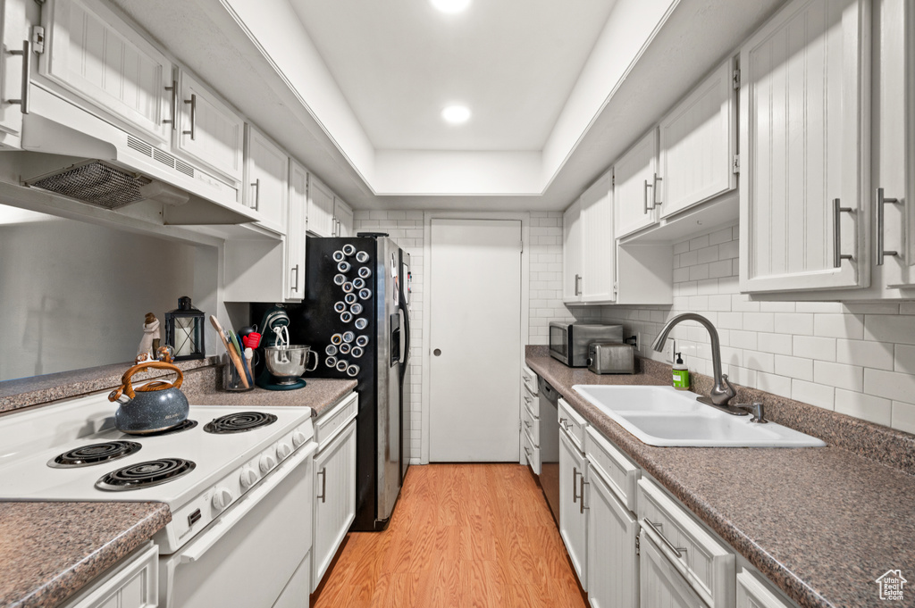 Kitchen with light wood-type flooring, white cabinetry, sink, tasteful backsplash, and white range with electric cooktop