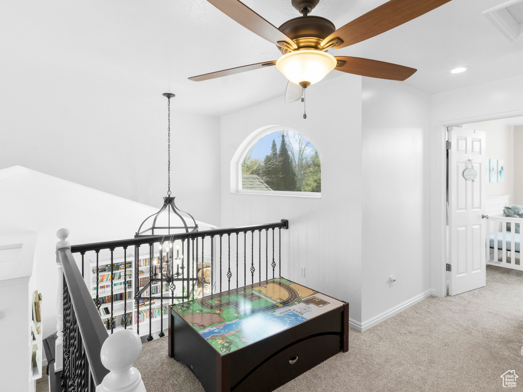 Living area featuring ceiling fan with notable chandelier and light colored carpet