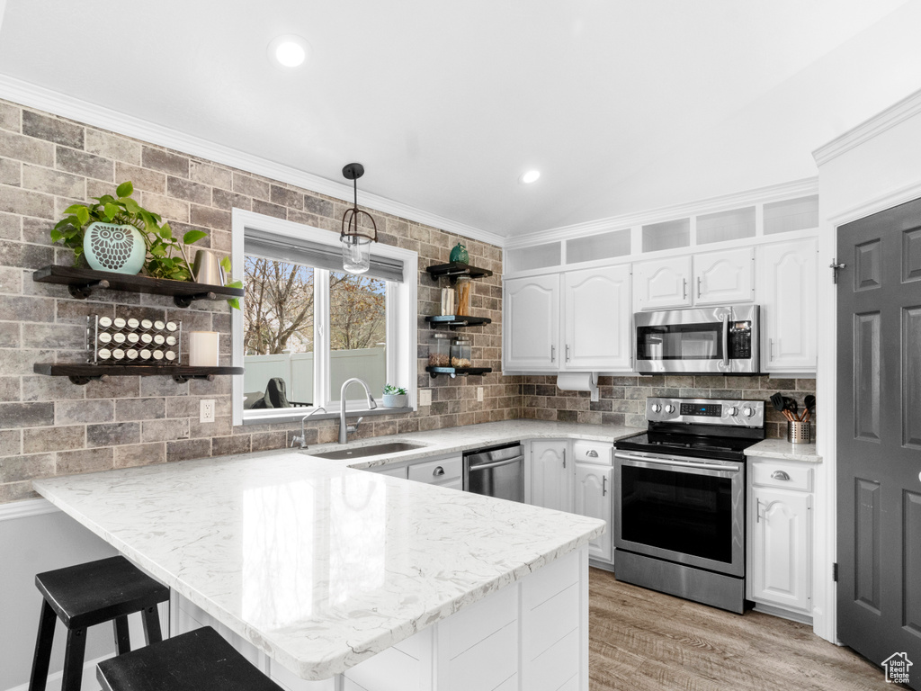 Kitchen with white cabinets, sink, a breakfast bar area, stainless steel appliances, and light hardwood / wood-style flooring