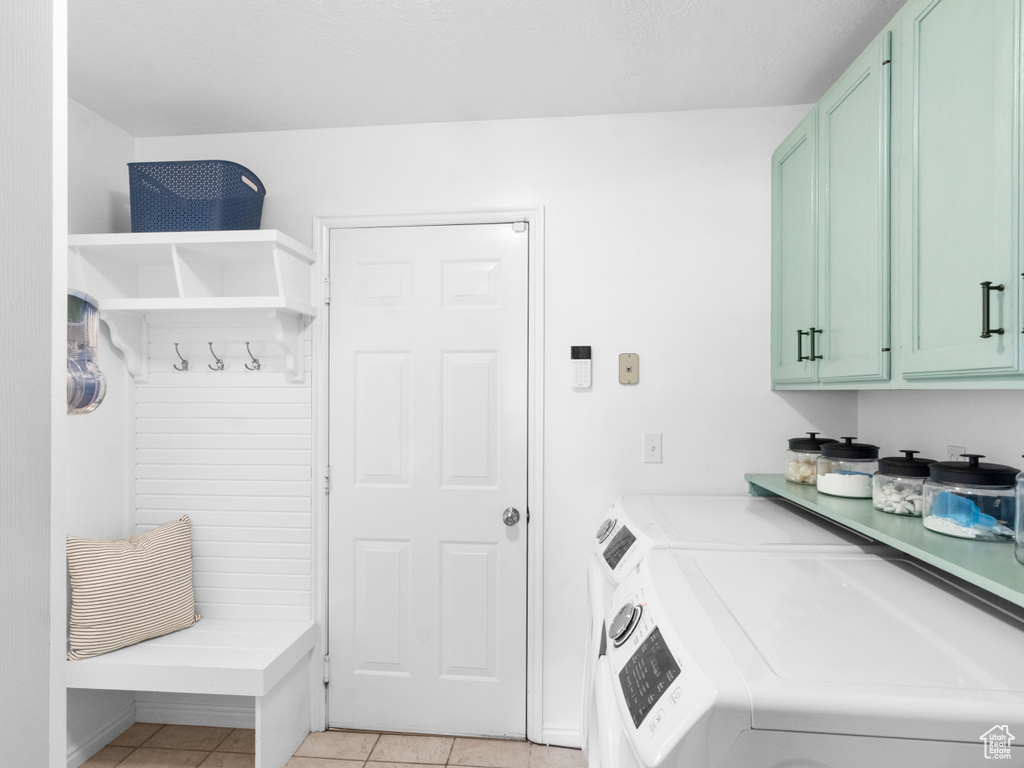 Laundry room featuring washing machine and dryer, cabinets, and light tile flooring