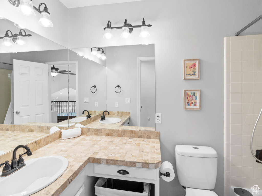 Bathroom featuring ceiling fan, toilet, and vanity with extensive cabinet space