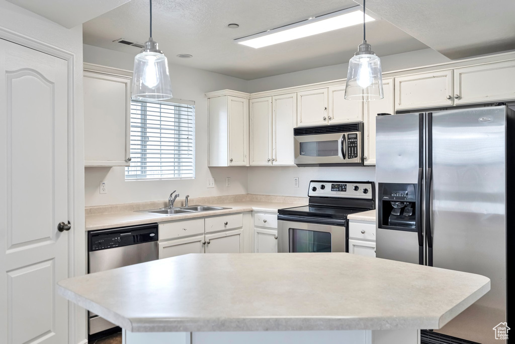 Kitchen featuring stainless steel appliances, white cabinets, sink, and decorative light fixtures