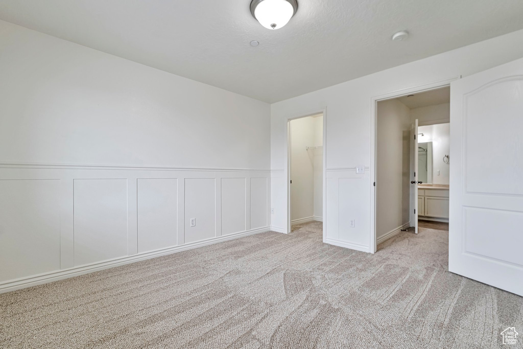 Unfurnished bedroom featuring a spacious closet, ensuite bath, light carpet, and a closet