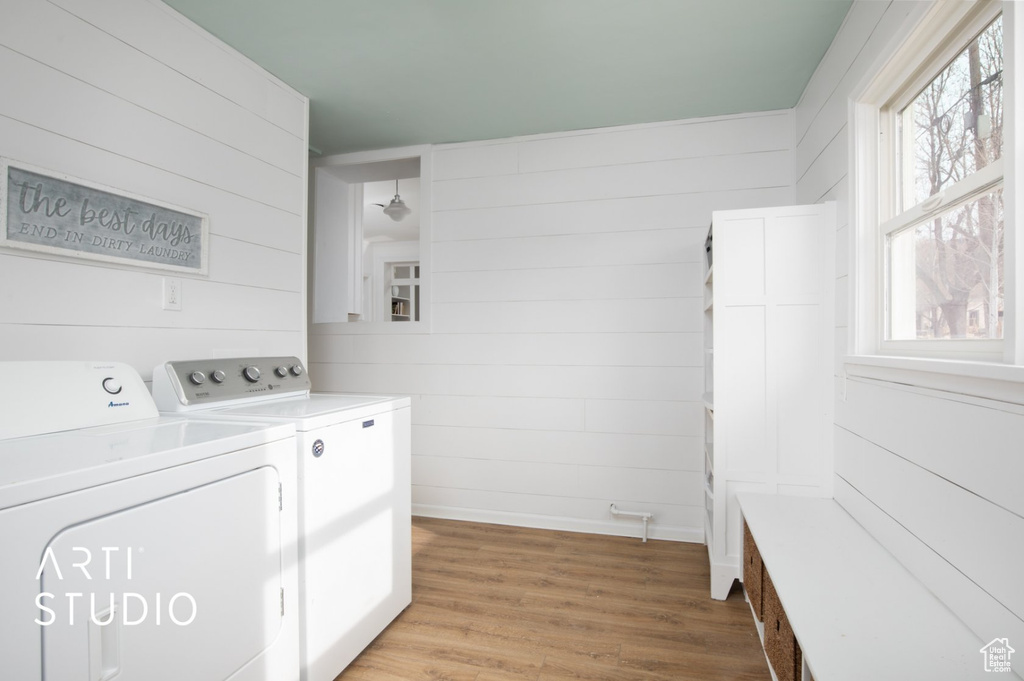 Washroom with wooden walls, light hardwood / wood-style floors, and washing machine and dryer