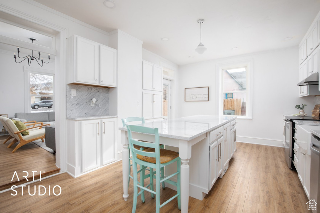Kitchen with white cabinets, decorative light fixtures, backsplash, and light wood-type flooring