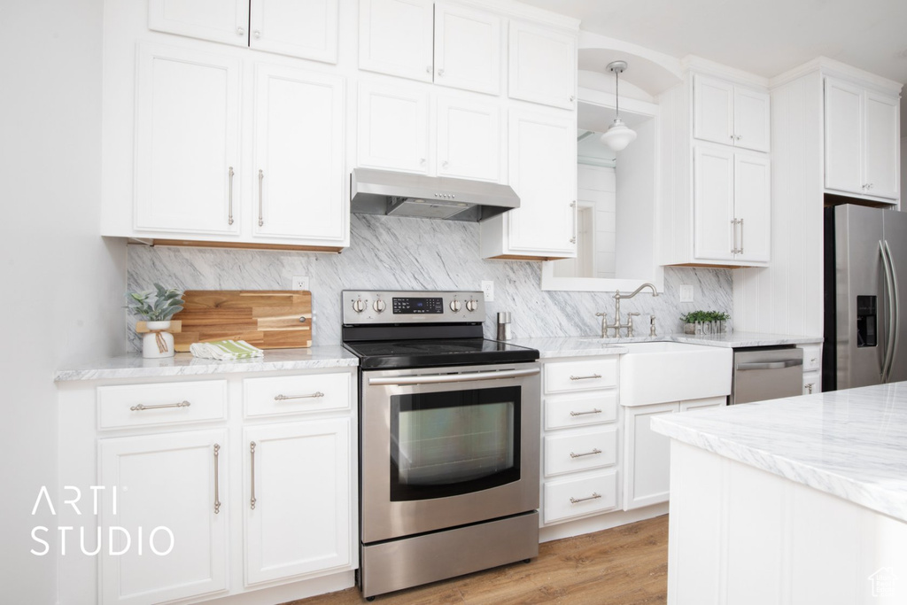 Kitchen featuring light stone counters, appliances with stainless steel finishes, fume extractor, light wood-type flooring, and white cabinetry