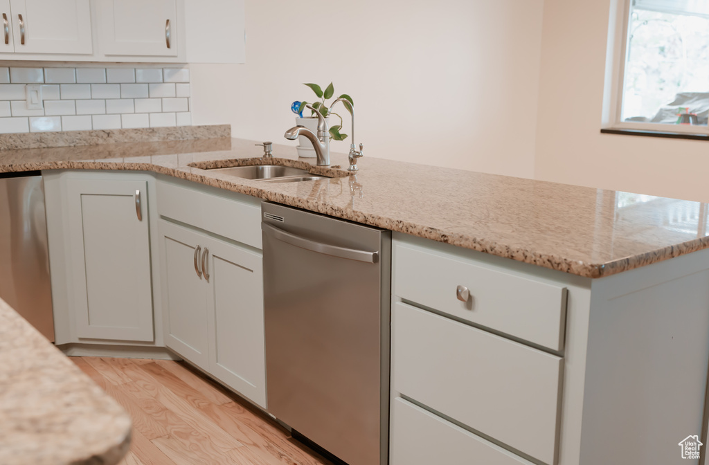 Kitchen featuring white cabinets, dishwasher, backsplash, light wood-type flooring, and light stone countertops