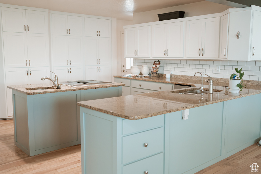 Kitchen with sink, light hardwood / wood-style floors, backsplash, and white cabinetry