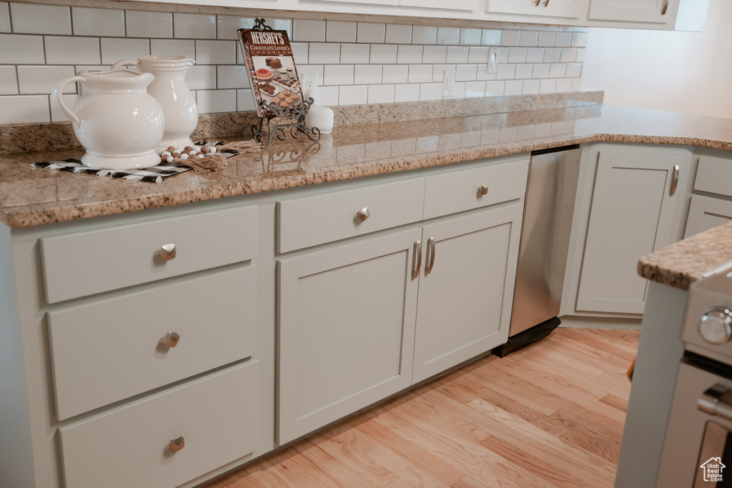 Kitchen featuring white cabinets, tasteful backsplash, light hardwood / wood-style floors, and light stone counters