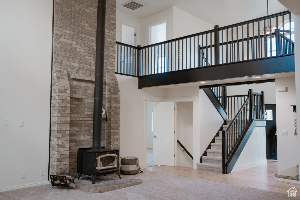 Staircase with light hardwood / wood-style floors, a towering ceiling, and a wood stove