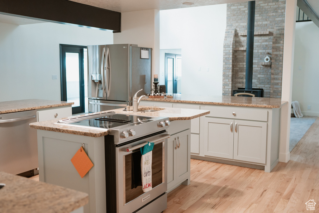 Kitchen featuring a wood stove, appliances with stainless steel finishes, light hardwood / wood-style floors, and a center island with sink
