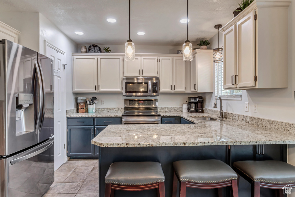 Kitchen featuring pendant lighting, appliances with stainless steel finishes, light tile floors, sink, and a breakfast bar area