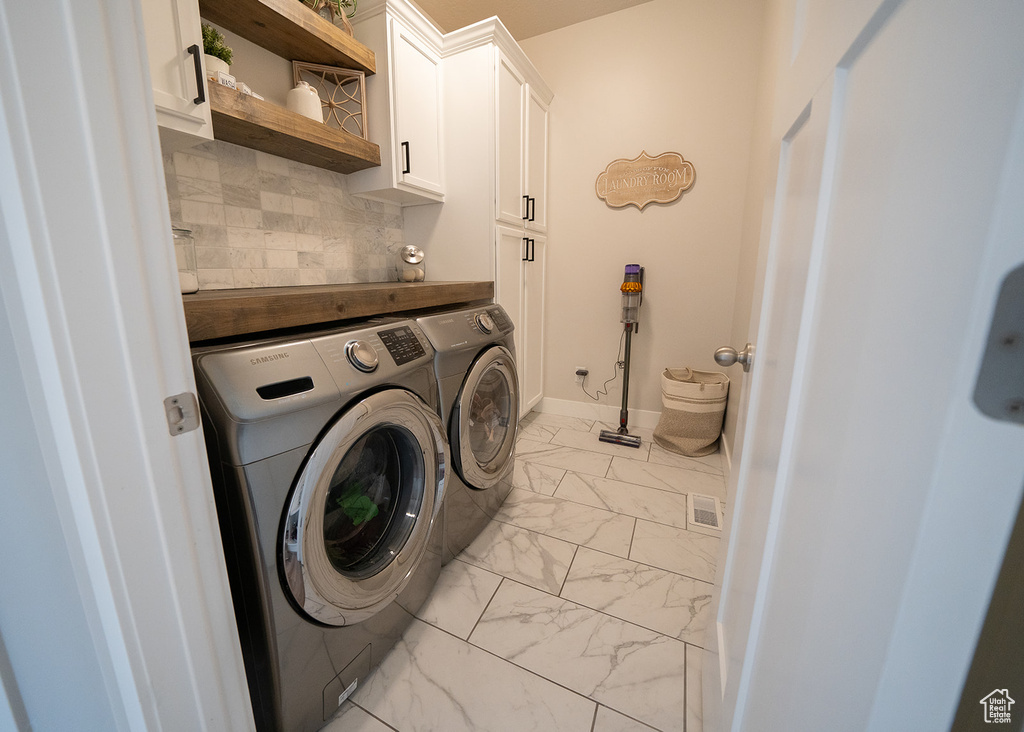 Washroom featuring washing machine and clothes dryer, cabinets, and light tile flooring