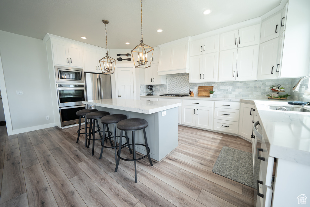 Kitchen featuring decorative light fixtures, white cabinets, appliances with stainless steel finishes, a kitchen island, and light hardwood / wood-style floors