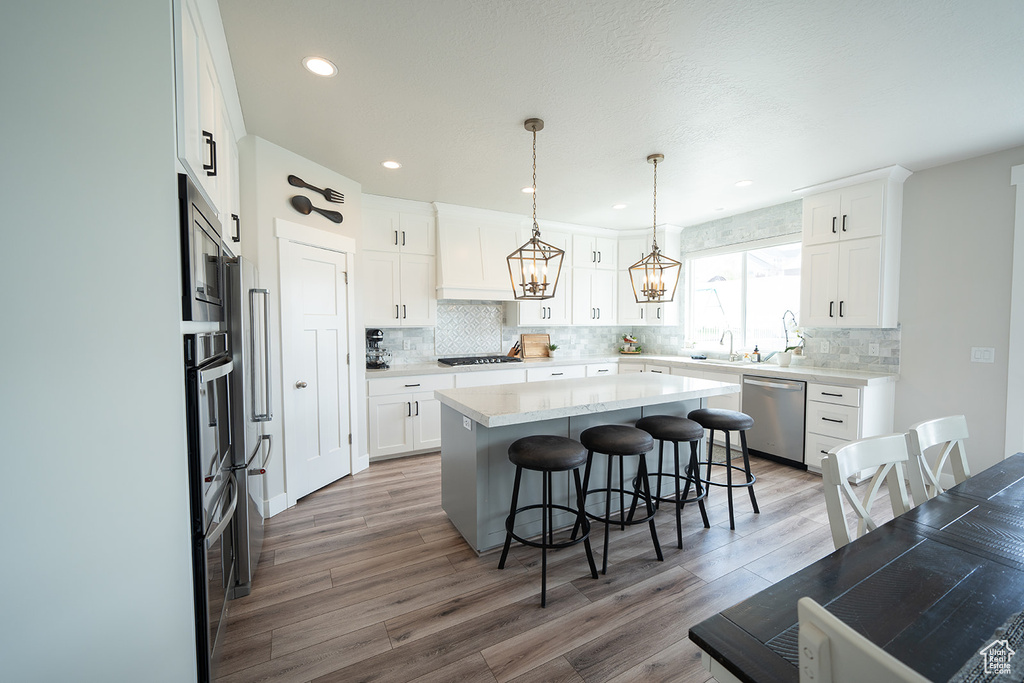 Kitchen with appliances with stainless steel finishes, pendant lighting, a kitchen island, and white cabinetry