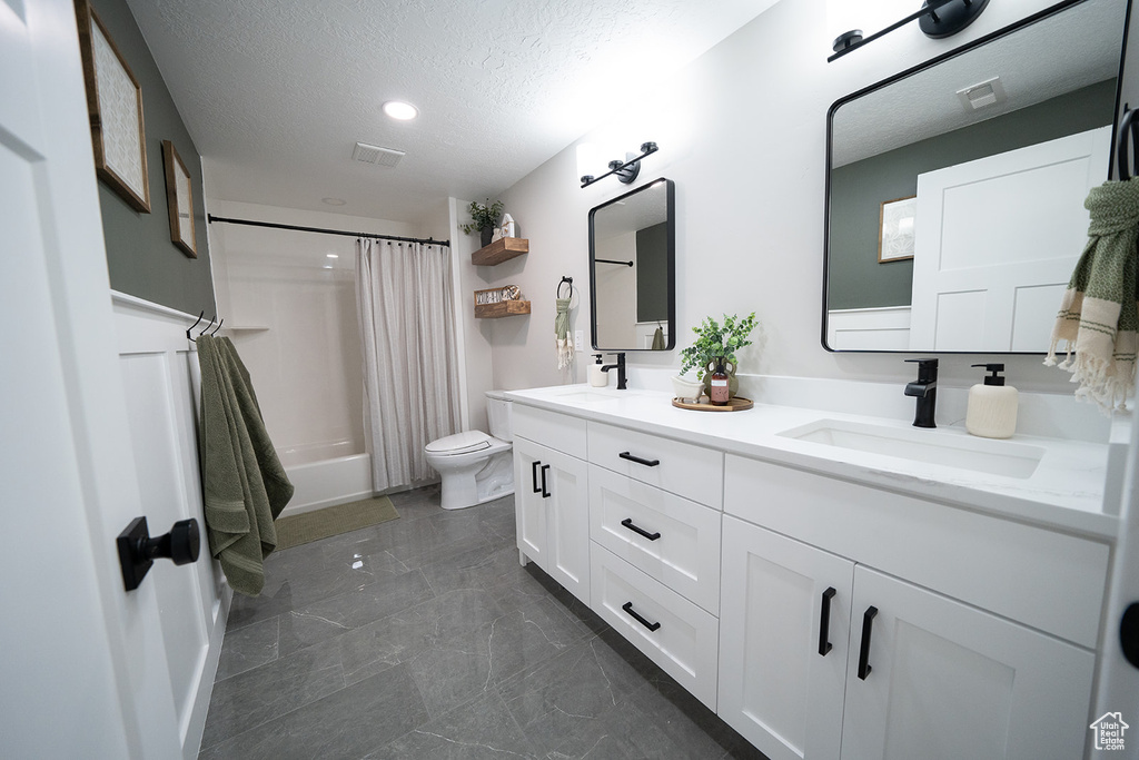 Full bathroom featuring a textured ceiling, double vanity, shower / bath combo, toilet, and tile floors