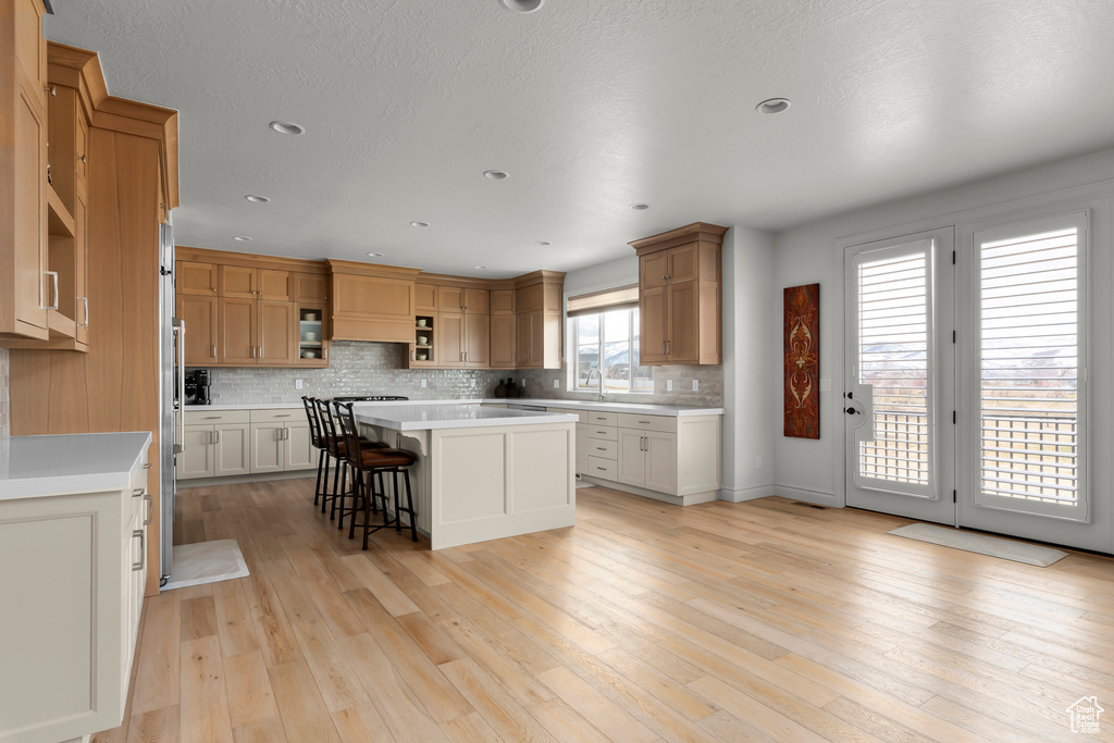 Kitchen with a center island, backsplash, light hardwood / wood-style floors, and a kitchen bar