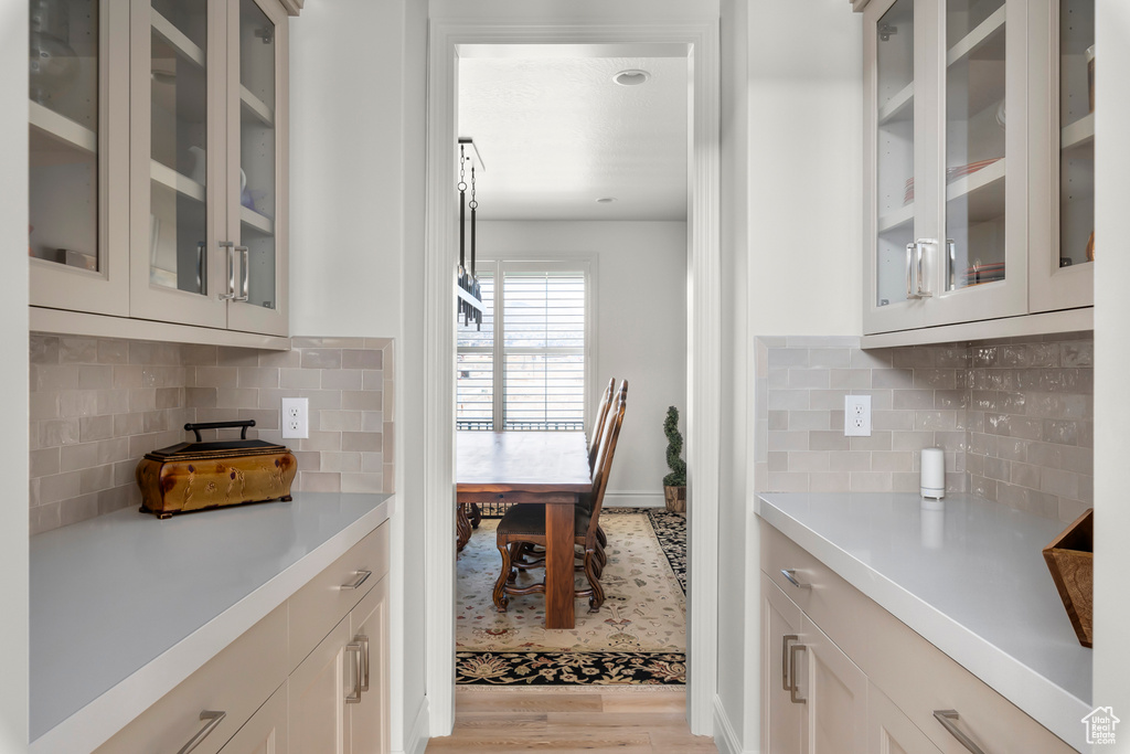 Kitchen with tasteful backsplash, light hardwood / wood-style flooring, and white cabinetry