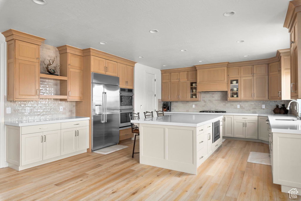 Kitchen with a center island, light hardwood / wood-style floors, tasteful backsplash, premium range hood, and built in appliances
